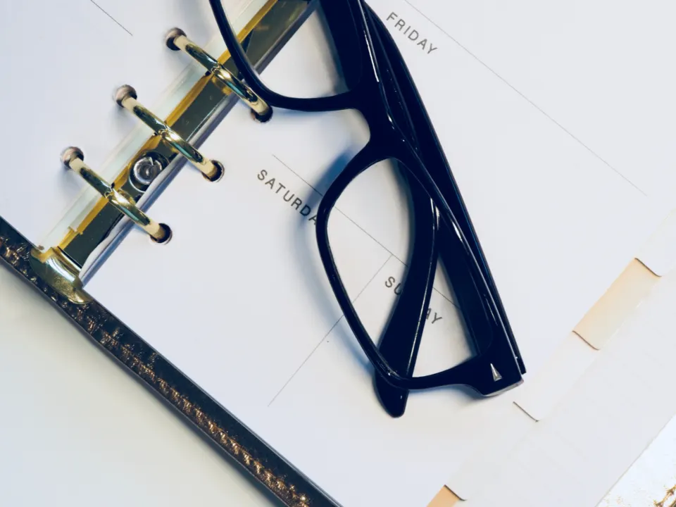 Reading glasses resting on an open ring-bound planner showing the days of the week