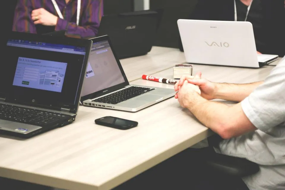 Colleagues at a shared desk with several laptops open, one screen showing a web application form